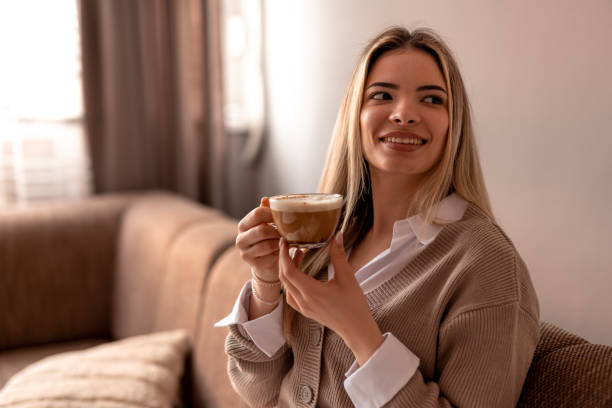 istock Smiling young woman drinking cappuccino at home on sofa 2190293879