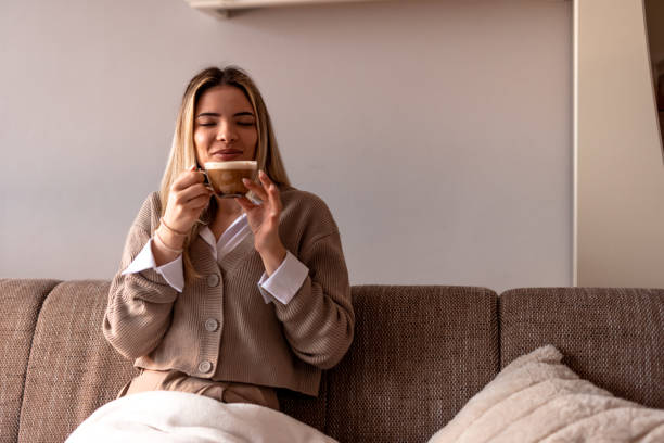 istock Smiling young woman drinking cappuccino at home on sofa 2190293884