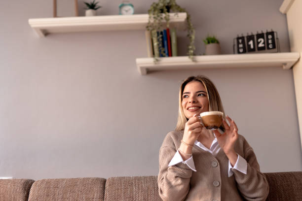 istock Smiling young woman drinking cappuccino at home on sofa 2190293888