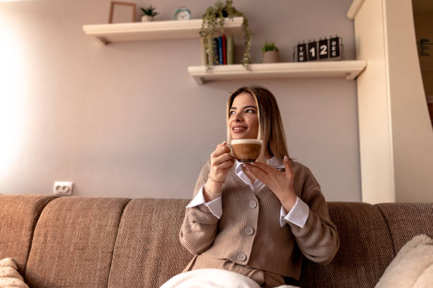 istock Smiling young woman drinking cappuccino at home on sofa 2190293899