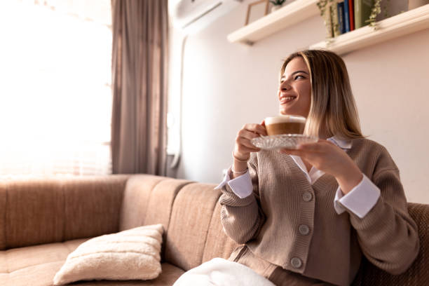 istock Smiling young woman drinking cappuccino at home on sofa 2190293914