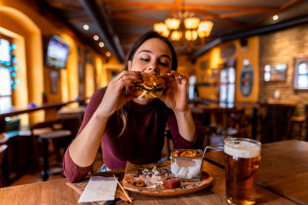 istock Young woman enjoying a burger and beer at a restaurant 2190296832