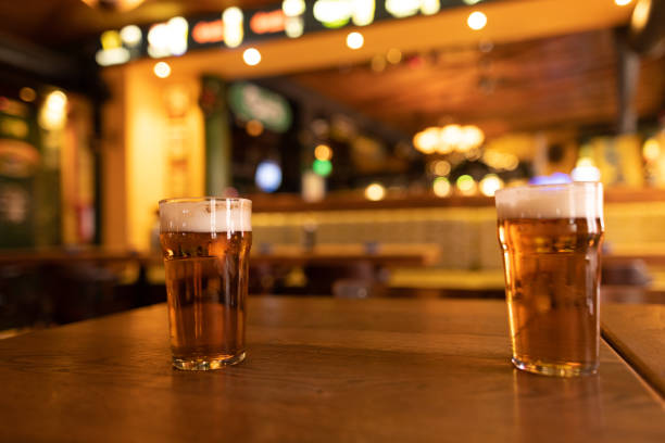 istock Two pint glasses of beer resting on table in bustling pub 2190296957