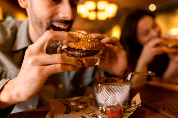 istock Man enjoying a delicious burger at a restaurant with friends 2190297105