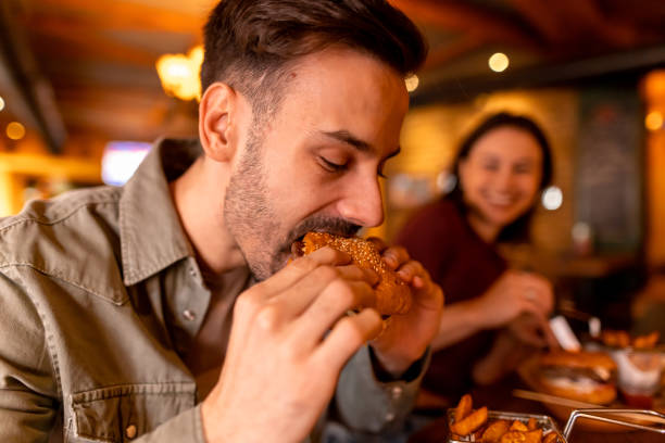istock Young man eating burger in restaurant with friend 2190297780