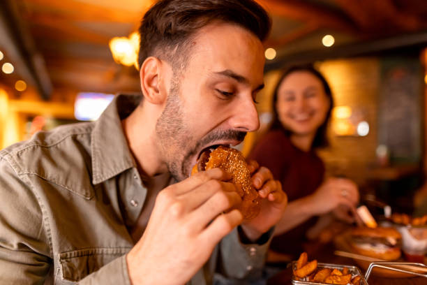 istock Young man enjoying a burger at a restaurant with a friend 2190297784