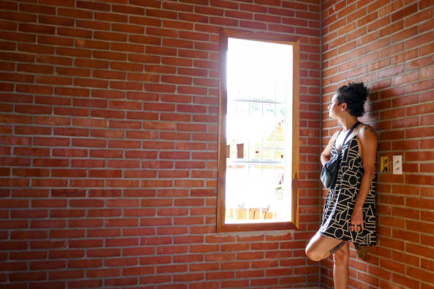 young woman is leaning against the wall looking at the window with closed eyes