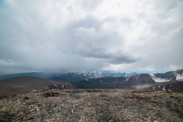 istock Dramatic top view from high stony pass to alpine valley against large mountain range with snow-capped peaks in gray rainy low clouds. Beautiful big snowy mountain tops in rain under grey cloudy sky. 2190303989