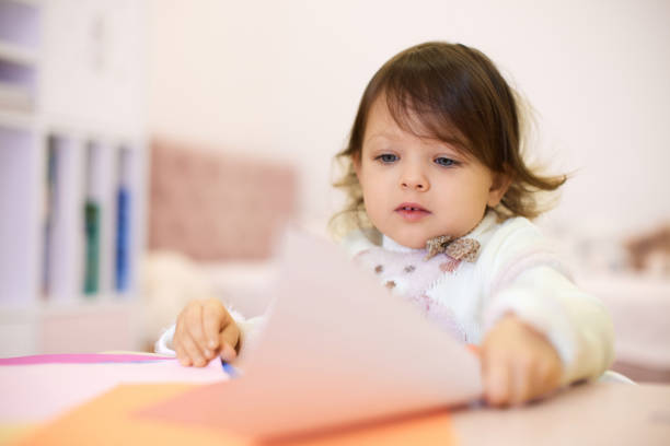 istock little child girl holding multi-color paper while sitting by table 2190306011