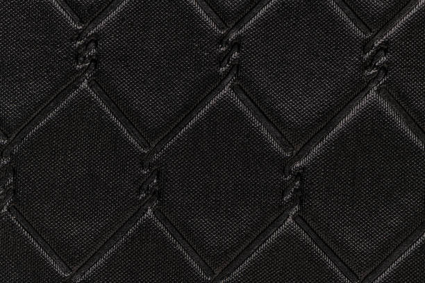 A close-up view of a black fabric with a raised, diamond-shaped latticework pattern. The pattern is created using a stitching technique that adds texture and depth to the fabric.