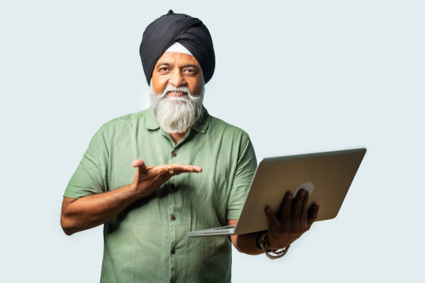 Indian Elderly Sikh man in casual wear using laptop while standing, showing confidence and success