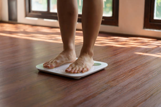 istock Fat diet and scale feet standing on electronic scales for weight control. Measurement instrument in kilogram for a diet control 2190328083