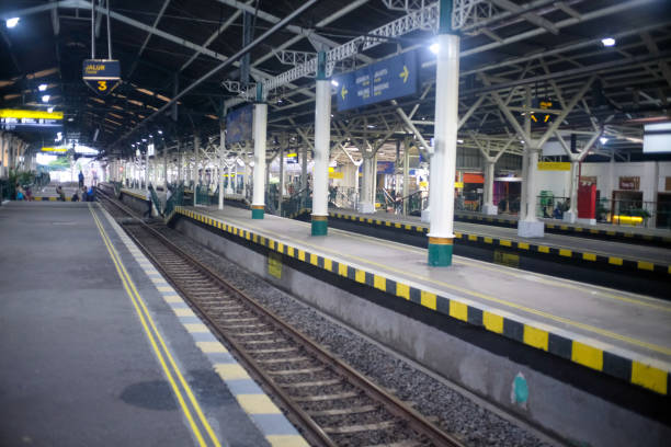 istock A train station platform with multiple tracks, highlighted by clear yellow safety lines and steel overhead roofing. Directional signs for train routes are visible, with a clean, organized layout. 2190333718
