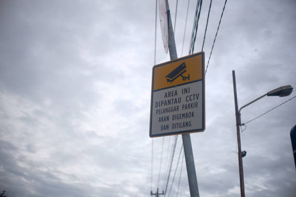 istock A warning sign with a yellow and white design stating that the area is monitored by CCTV, and parking violations will result in clamping and fines. The sign is mounted on a pole against a cloudy sky. 2190334323