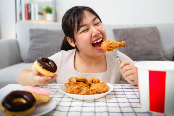 istock A beautiful Asian woman eats fried chicken and donuts with a smile on her face. 2190337877