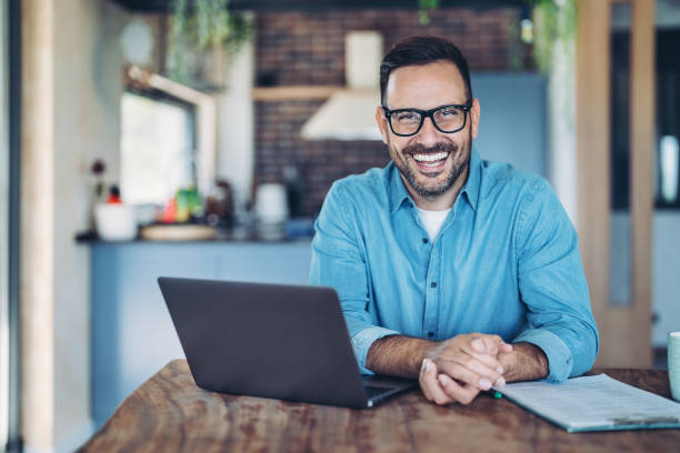 istock Smiling man with laptop and paperwork in a domestic kitchen 2190340734