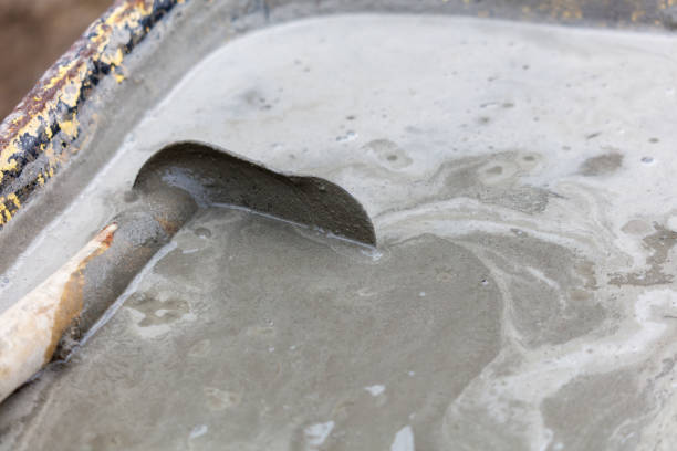 A person is using a shovel to mix concrete in a tray