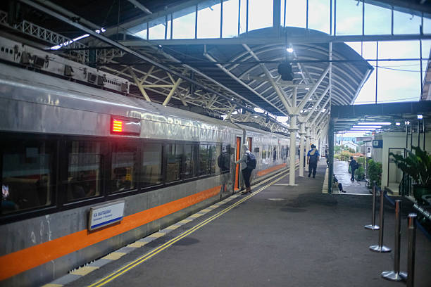 istock A passenger train stationed at a platform under a modern, covered structure with steel beams and a high ceiling. A person is boarding the train, while others are walking along the platform. 2190345249