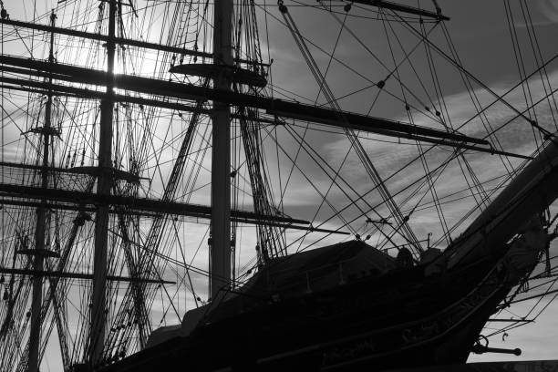 An old wooden boat resting on calm water at night, illuminated by distant lights, in black and white