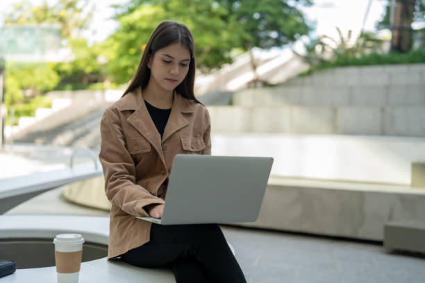 istock young woman working on laptop outdoors, focused and engaged. She is seated at modern table with coffee cup nearby, surrounded by greenery 2190353944