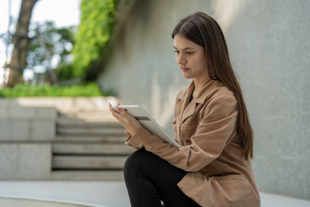 istock young woman sitting on steps, using tablet in serene outdoor setting. She wears brown jacket and appears focused and engaged 2190353965