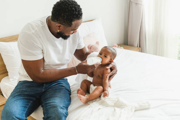 istock A caring father feeds his baby on a bed, showcasing a warm and nurturing moment between parent and child. Happy diversity family and newborn bathing concept. 2190354554