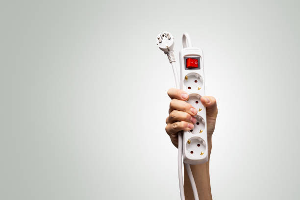 A hand holding a European-style power strip with multiple sockets, plug, and a red switch, isolated on a neutral background with copy space.