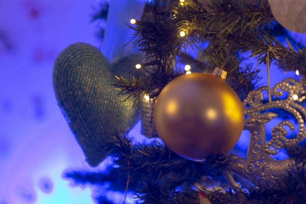 A closeup view of a beautifully adorned Christmas tree, showcasing various decorations, with a shimmering gold ball gracefully hanging from its branches