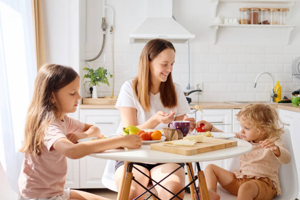 istock A mother sits at a round table with her two children in a sunny kitchen, sharing breakfast and engaging in conversation while surrounded by fresh fruit 2190367692