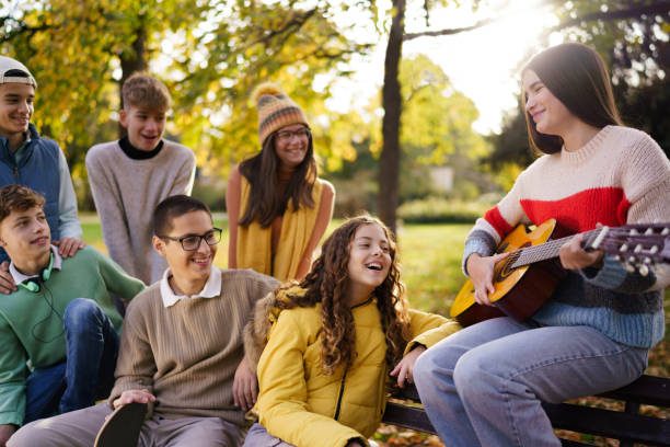 istock Teenagers having fun while their friend playing a guitar in the park 2190367697