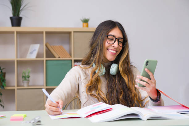 istock Young woman studying at home, taking notes from her smartphone 2190378035