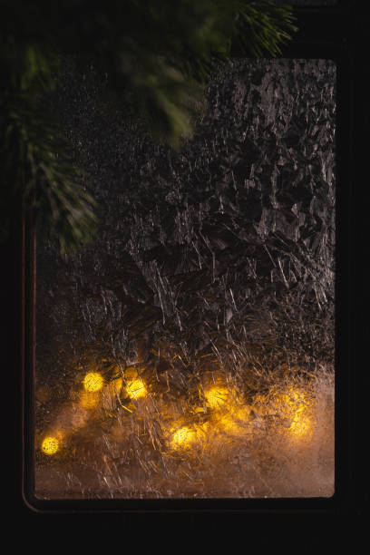 istock Warm christmas lights shining through a frozen window with visible ice crystals and a pine tree branch in the foreground creating a cozy winter atmosphere 2190378745