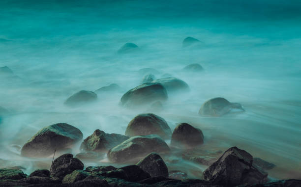 Long exposure photograph of ocean waves crashing on mossy rocks at twilight, creating a misty, ethereal scene in vila nova de gaia, portugal