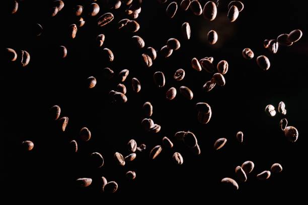 Roasted coffee beans falling against black background