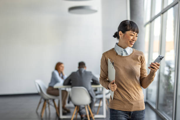 istock Modern smiling Japanese businesswoman using smartphone in office 2190396090