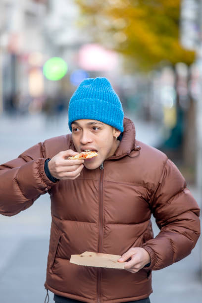 istock Young man taking a bite of pizza while enjoying a cold urban morning 2190402830