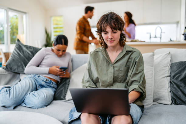 Young Transgender Boy Using Laptop While Sitting In The Living Room In Sydney In Australia Young transgender boy using laptop while sitting in the living room in Sydney in Australia. His family in the background. trans boy stock pictures, royalty-free photos & images