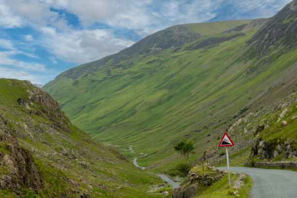 Descend of the B5289 road with sign of 25% steep grade from Honister Pass in the Lake District, Cumbria, UK surrounded by green mountains with pasture
