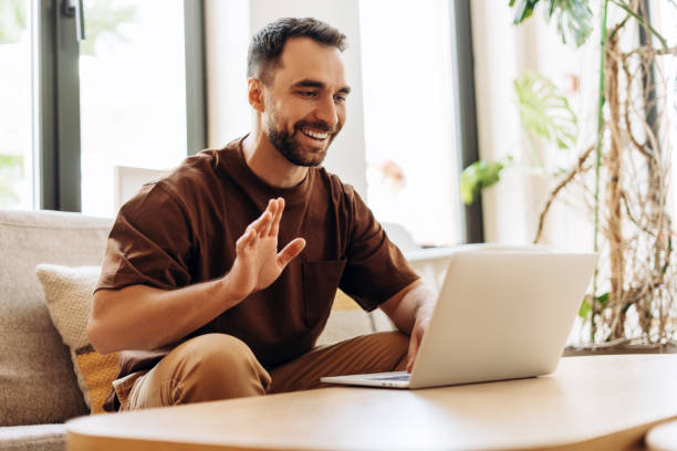 Handsome young Hispanic man, freelancer using laptop, having video call, waving hand