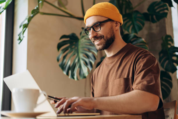 istock Smiling, happy, confident man, hipster wearing yellow hat, holding digital tablet, using laptop 2190416391