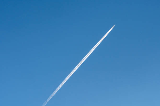 A jet leaves a long white contrail against a bright blue sky, creating a striking contrast. The daylight highlights the clarity and depth of the atmosphere.
