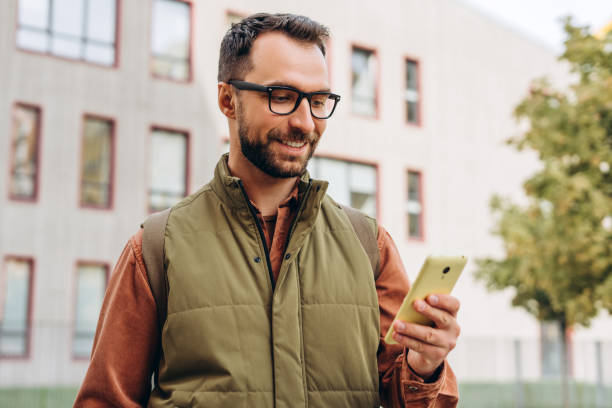 istock Smiling, bearded, Latin man wearing eyeglasses holding mobile phone, using mobile app, text message 2190417952