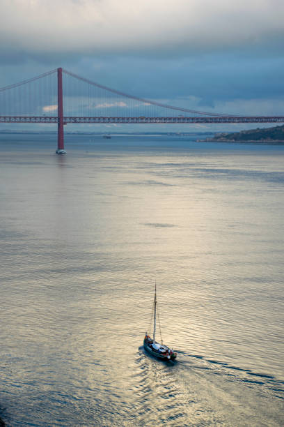 Scenic view of a sailboat sailing on the tagus river with the iconic 25 de abril bridge in the background, lisbon, portugal