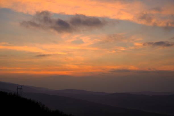 Captivating scene depicting a colorful sunset sky over hilly terrain, exuding tranquility and beauty.
