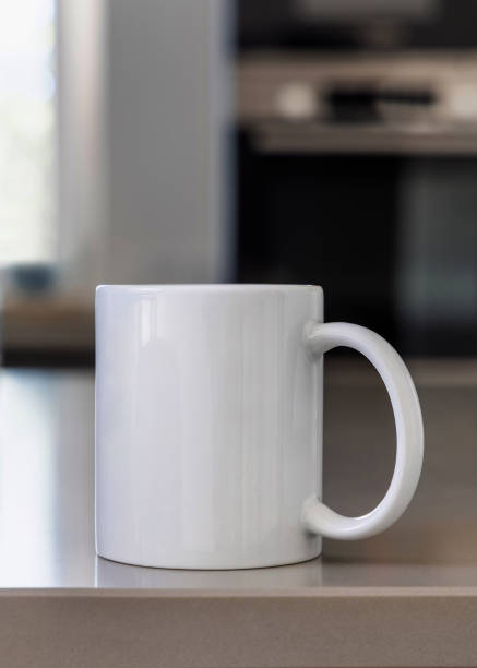 istock Closeup of  white blank coffee mug on grey kitchen table over blured kitchen interior, mockup 2190427294