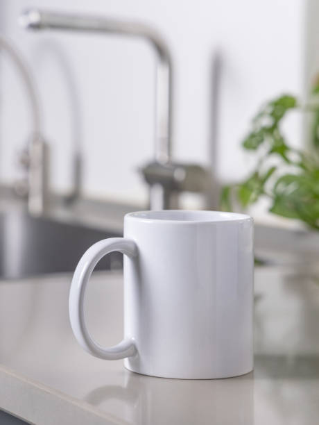 istock White coffee mug on grey kitchen table against kitchen interior with sink, closeup, mockup 2190427295