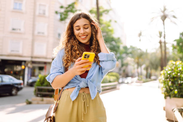 istock Smiling young woman walking around old street using smartphone. 2190429315