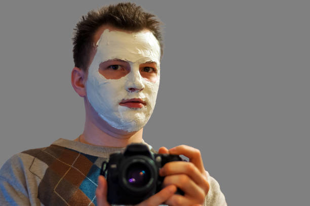Man taking a self-portrait with a face mask, a mix of humor and unusual expression. Combining beauty routines with casual self-portraiture.