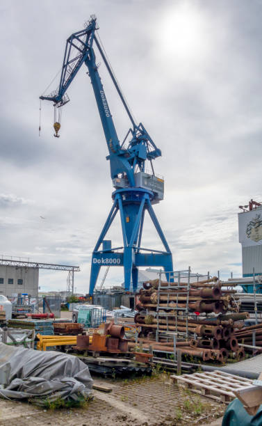 A large dockyard crane - Dok8000 Kran - which is part of Dok8000, a commercial centre in the docks area of Aarhus, a port city in eastern Jutland, Denmark. In the foreground is part of a reclamation yard filled with old construction and industrial equipment.