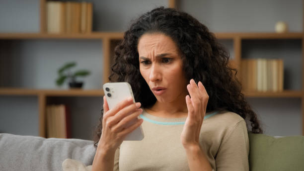 istock Hispanic sad displeased woman has problem with online mobile app on cell phone unhappy with blocked account in social networks looking at cellphone screen scam unsuccessful bad news sitting at home 2190435764